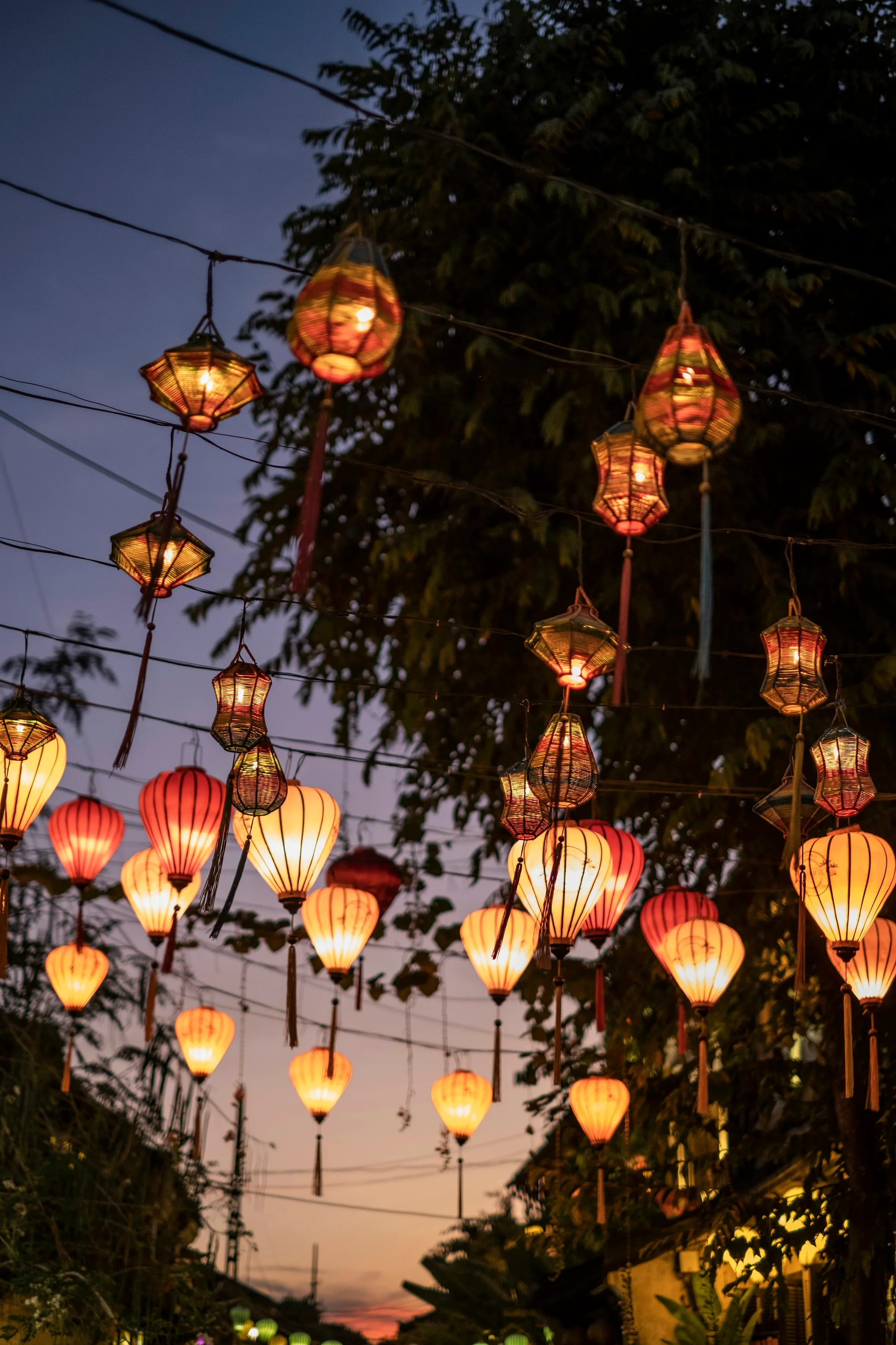 Glowing silk lanterns strung over a street in Hoi An at dusk